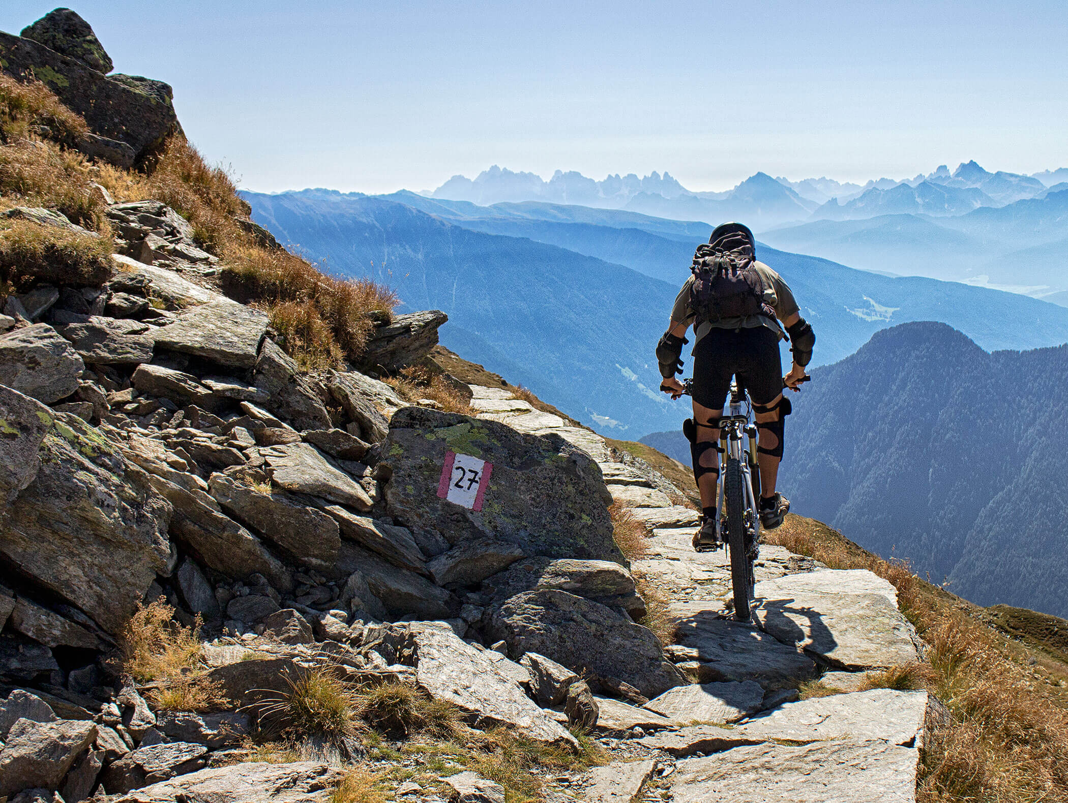 Un mountain biker su un sentiero sottile e sassoso, con le montagne altoatesine sullo sfondo - Pensione Oberwirt