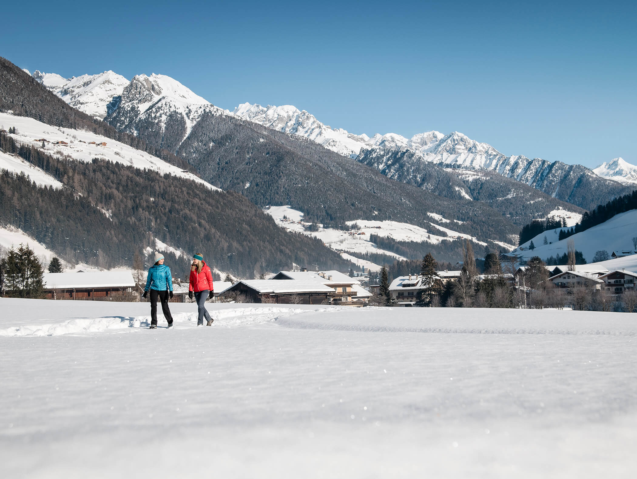 Due donne camminano nella neve fresca a Selva dei Molini, montagne innevate sullo sfondo - Pensione Oberwirt
