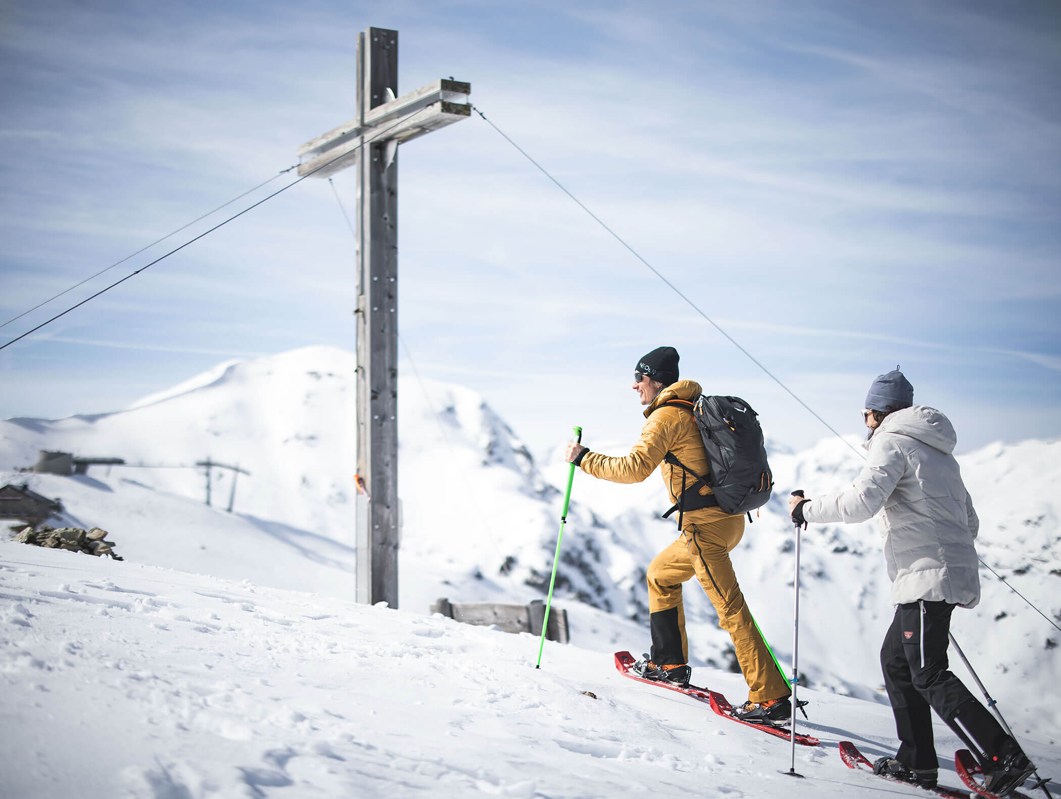 Due escursionisti con le racchette da neve passano davanti alla croce di legno della vetta - Pensione Oberwirt